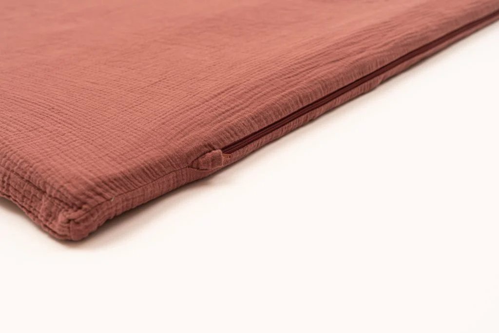 Dettaglio del bordo di un tappetone color mattone, con la cerniera della fodera in mussola