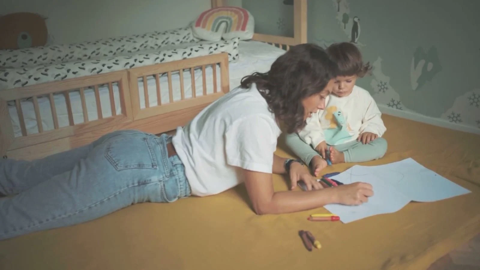 Una donna e una bambina disegnano sdraiate su un tappetone senape nella cameretta